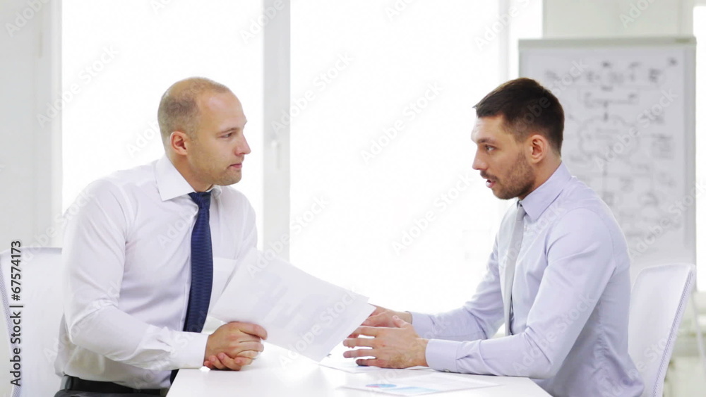 two serious businessmen with charts in office two serious businessmen with charts in office
