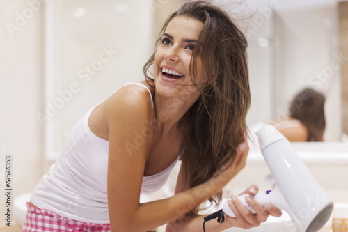 A young woman blow drying her hair in bathroom