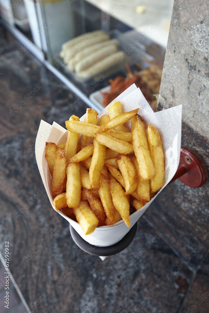 Potatoes fries in a little white paper bag hanging at the wall f Potatoes fries in a little white paper bag hanging at the wall f