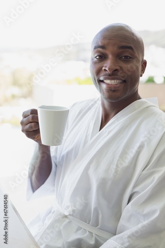 Handsome man in bathrobe drinking coffee outside