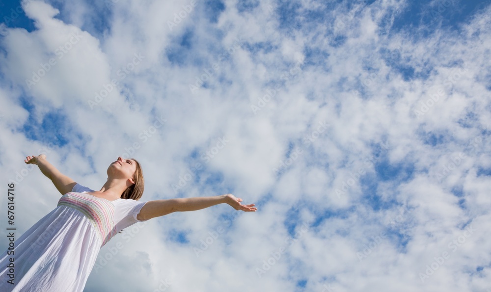 Woman with arms outstretched against blue sky and clouds