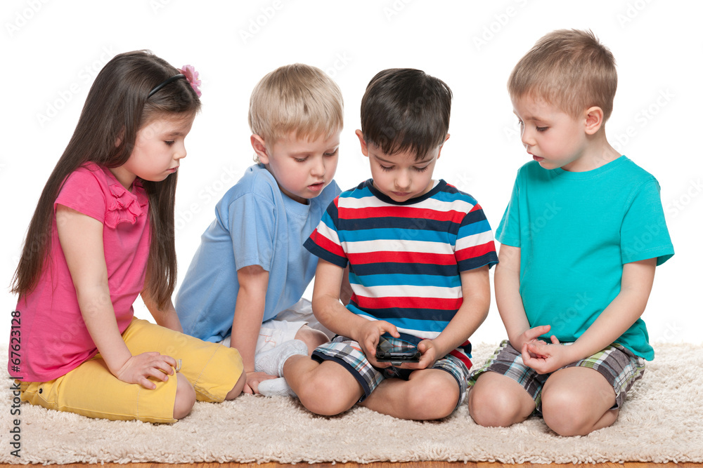 Fototapeta premium Four kids with a gadget on the carpet
