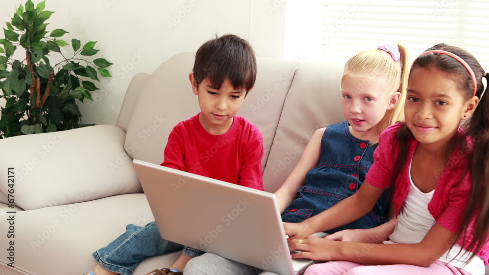 Three cute children using laptop together on the sofa Three cute children using laptop together on the sofa