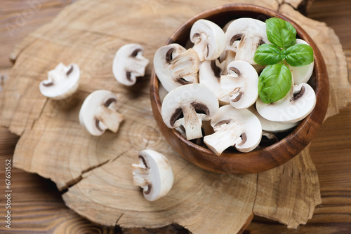 Raw sliced champignons and green basil over wooden background
