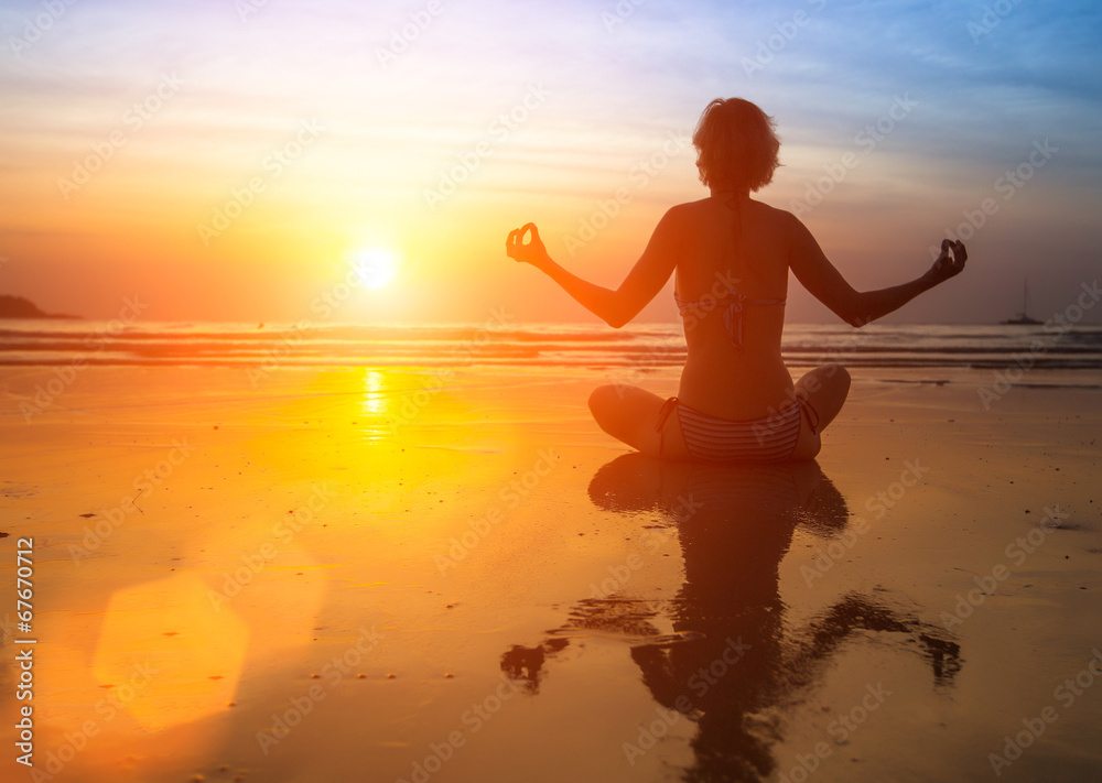 Yoga woman sitting on sea coast at sunset.