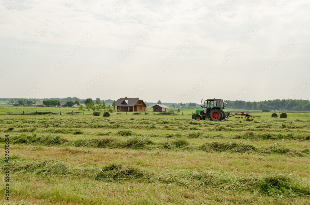 tractor turning raking cut hay in field