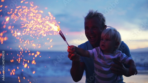Father and son lighting sparklers on the beach at sunset