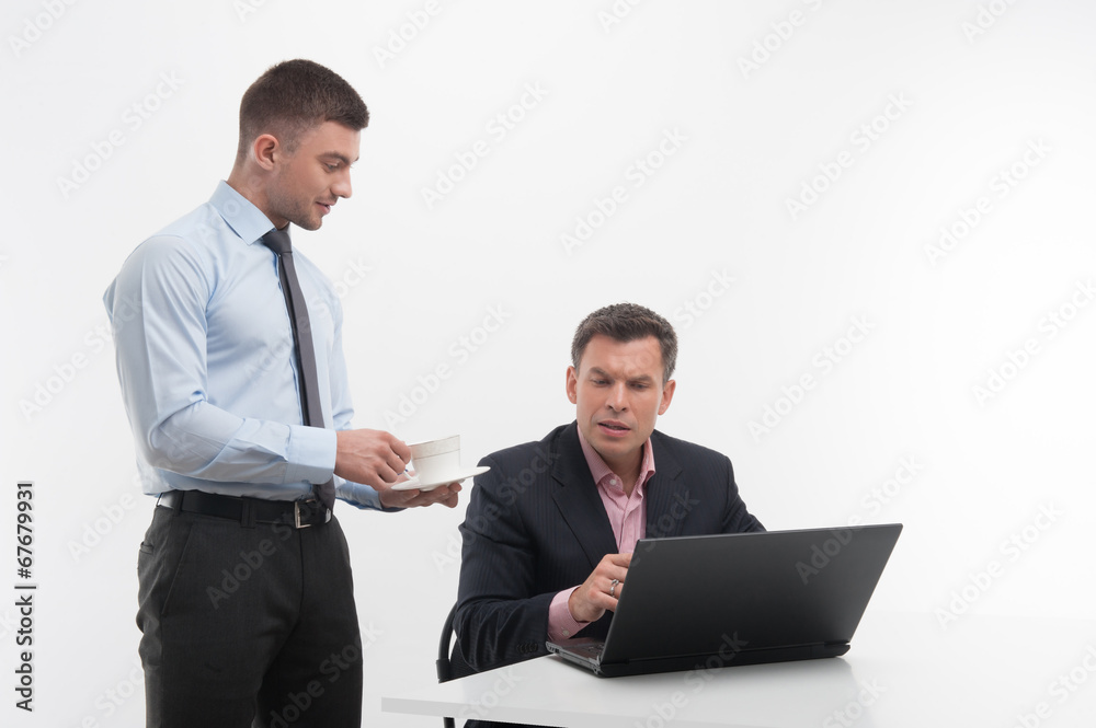 Young handsome office worker assistant brings coffee cup to seni Young handsome office worker assistant brings coffee cup to seni