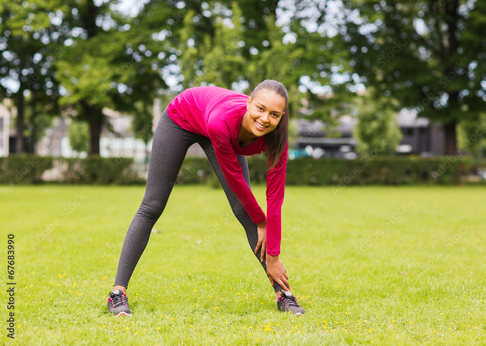 smiling black woman stretching leg outdoors