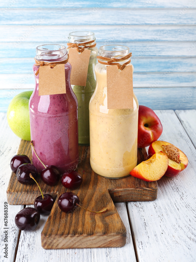 Obraz premium Assorted fruit smoothies in glass bottles with blank labels, fresh fruits, and wooden board on rustic table