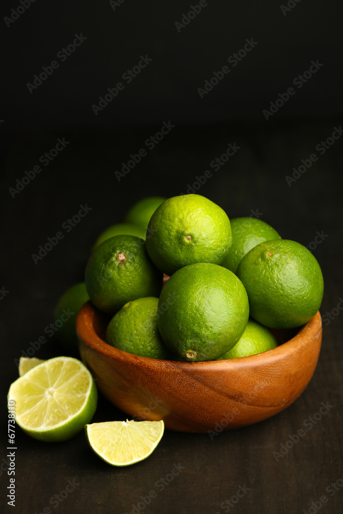 Fresh juicy limes in wooden bowl, on dark background Fresh juicy limes in wooden bowl, on dark background