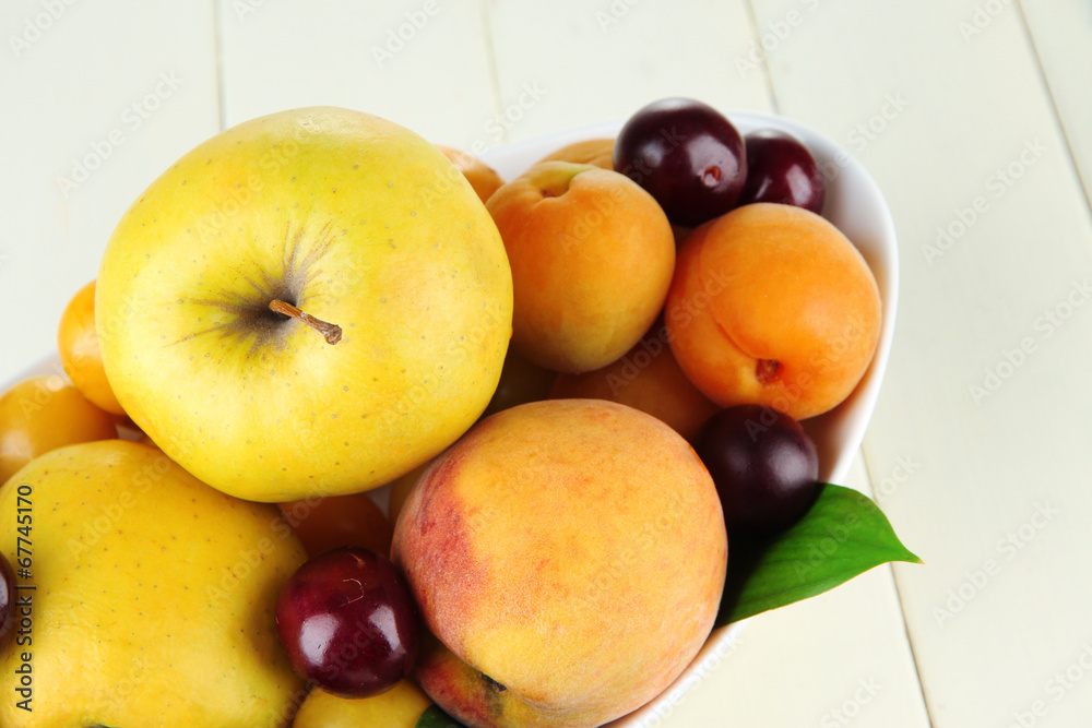 Bright summer fruits in plate on wooden table close-up
