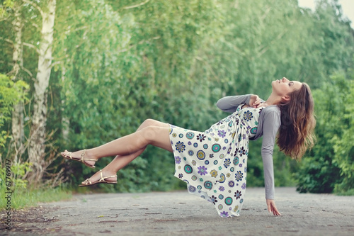 Fotografi Young brunette girl in colorful dress levitating in the park
