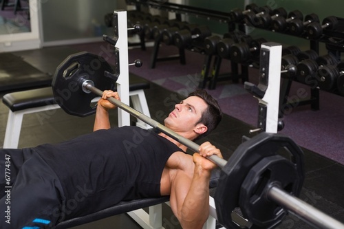 Determined muscular man lifting barbell