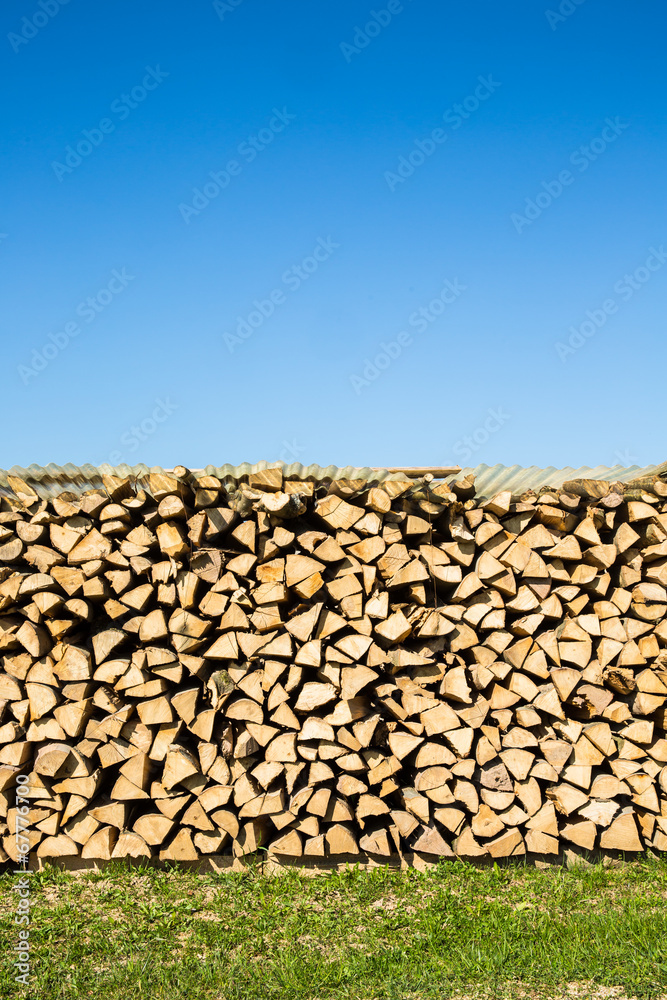 Pile of chopped firewood with green grass and blue sky