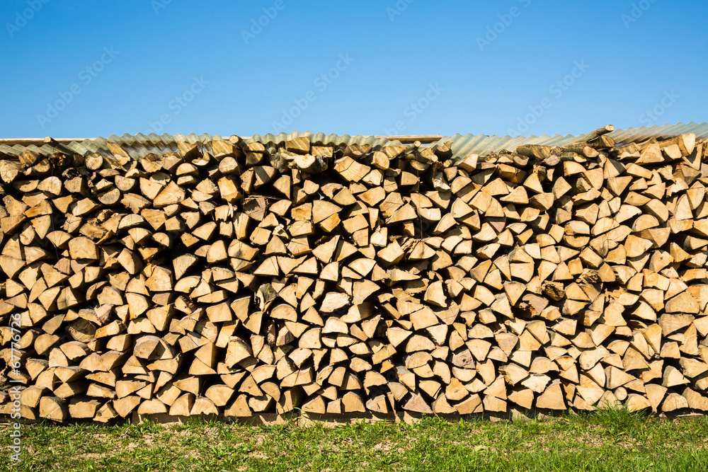 Pile of chopped firewood with green grass and blue sky