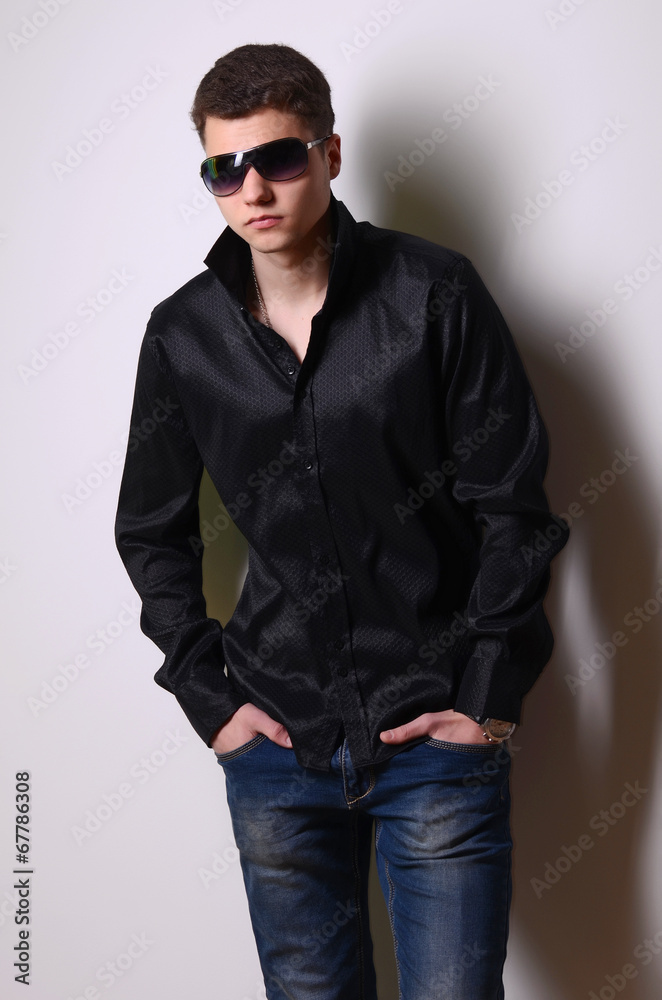Plakat Fashion portrait of young man in black shirt poses over wall