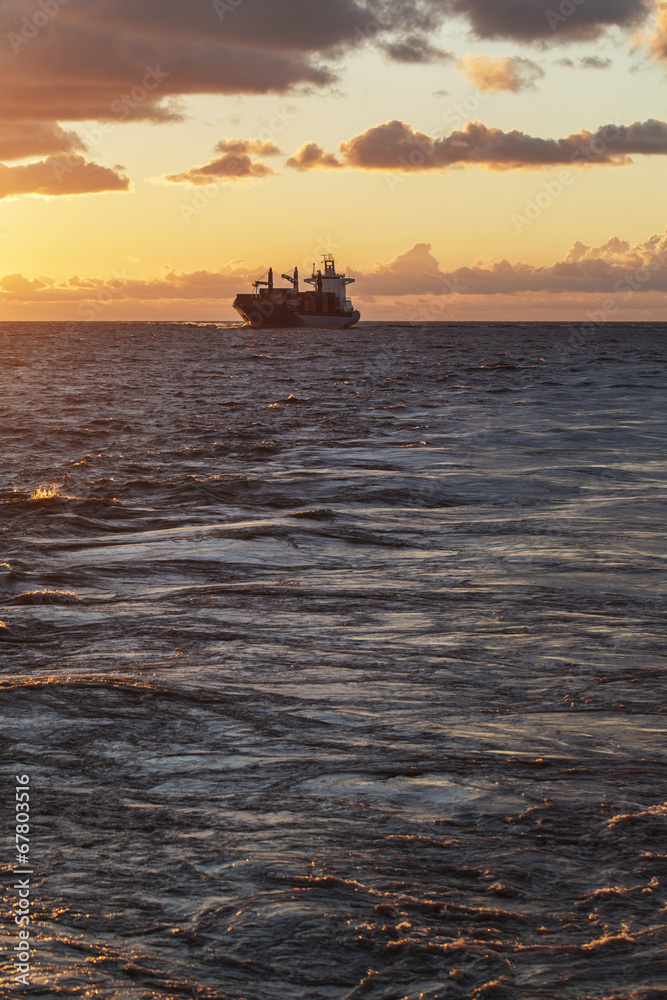Obraz premium Cargo ship underway at sunset