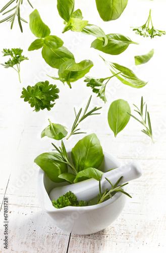 green herbs falling into mortar and pestle