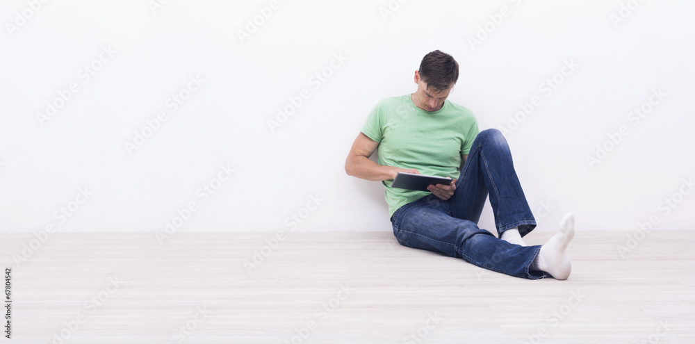 Fototapeta premium man using a tablet pc sitting in front of white wall.