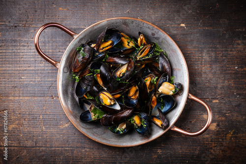 Boiled mussels in copper cooking dish on dark wooden background