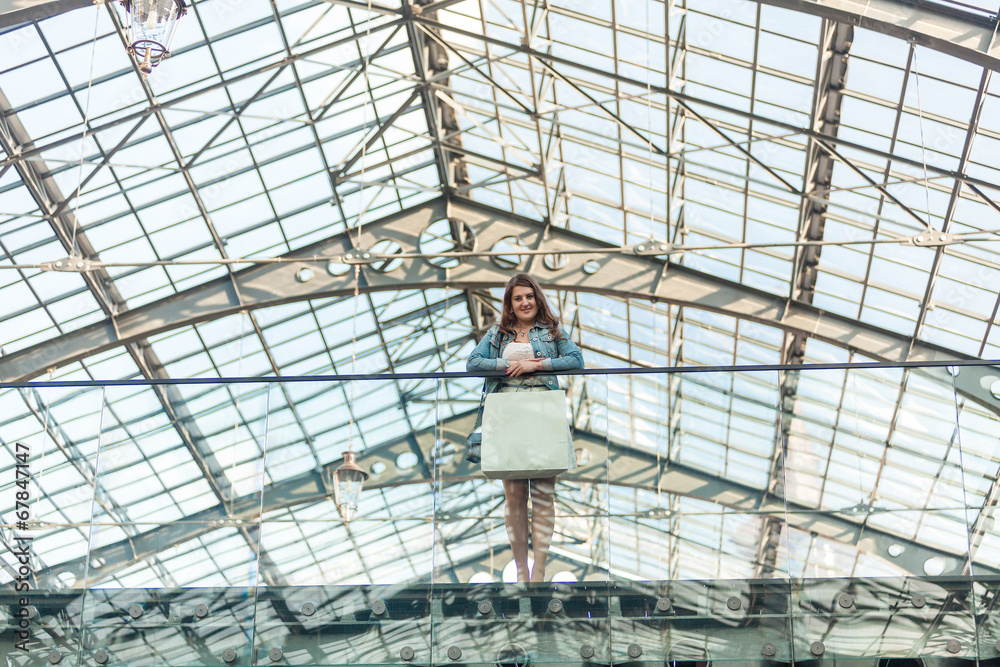 woman with white paper bag standing at mall with glass ceiling