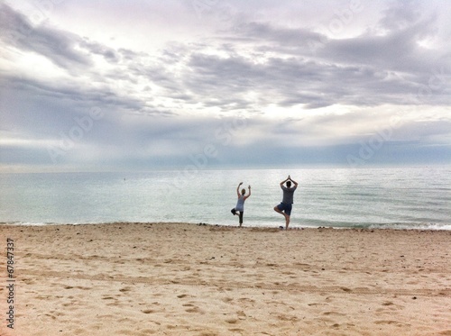 two people practicing yoga on the beach