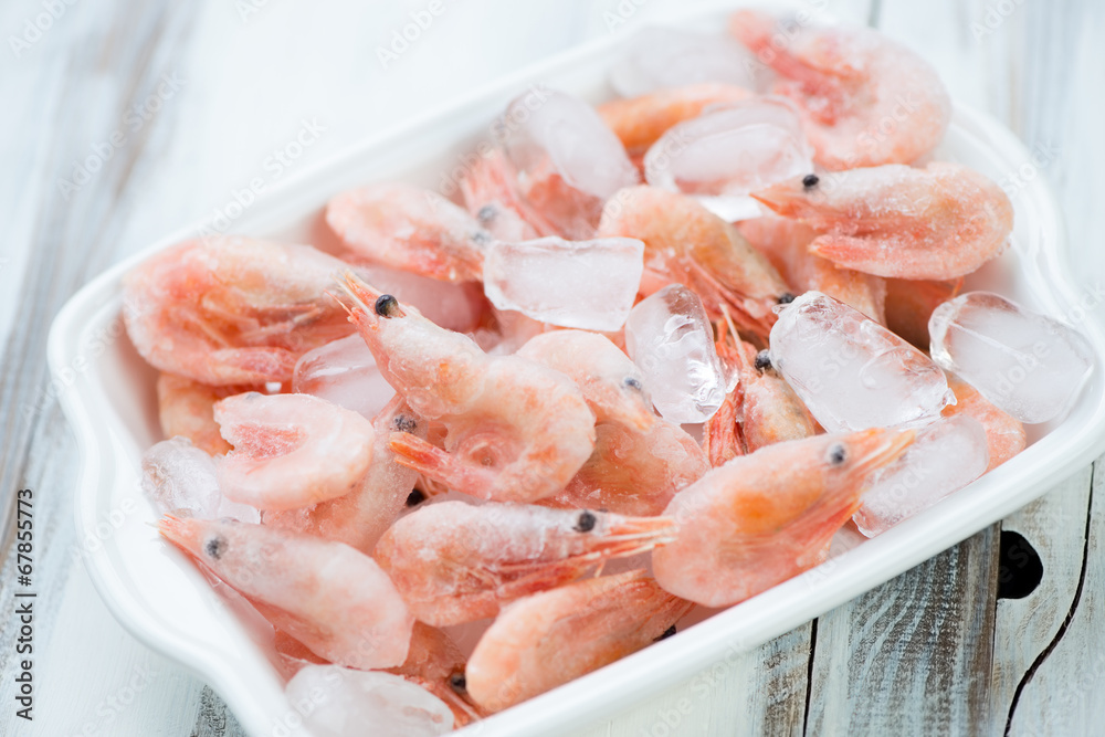 Glass bowl with raw frozen shrimps on ice cubes, high angle view Glass bowl with raw frozen shrimps on ice cubes, high angle view