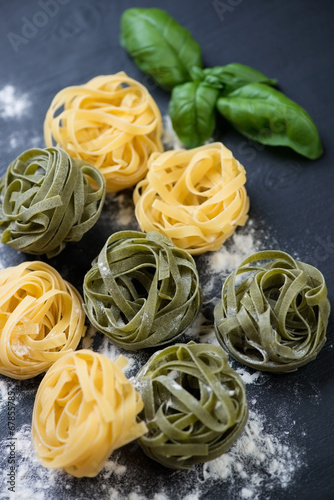 Colored tagliatelle with green basil leaves, high angle view
