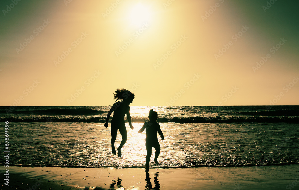 two happy kids playing on the beach at sunset