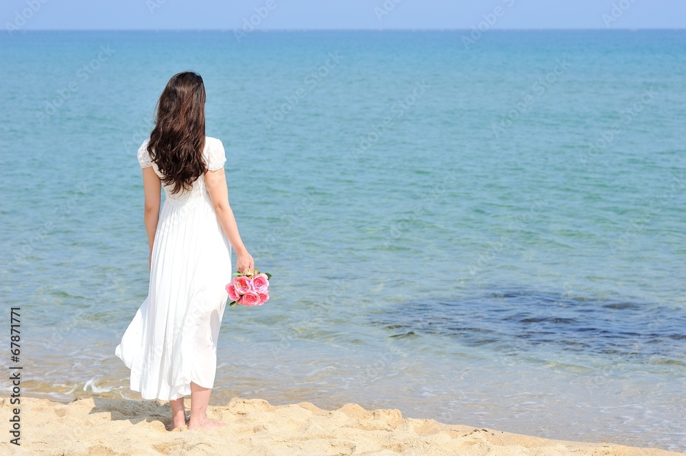 白いワンピースを着てピンクの花束を持って海に向かって立っている女性