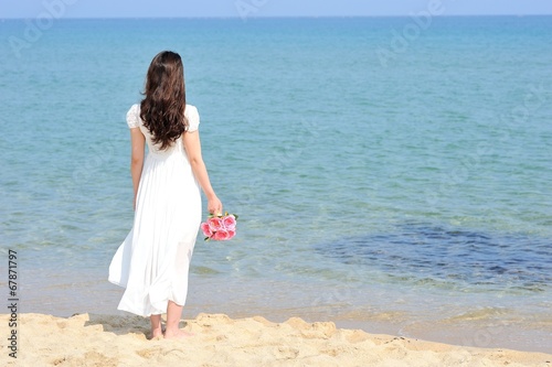 白いワンピースを着てピンクの花束を持って海に向かって立っている女性