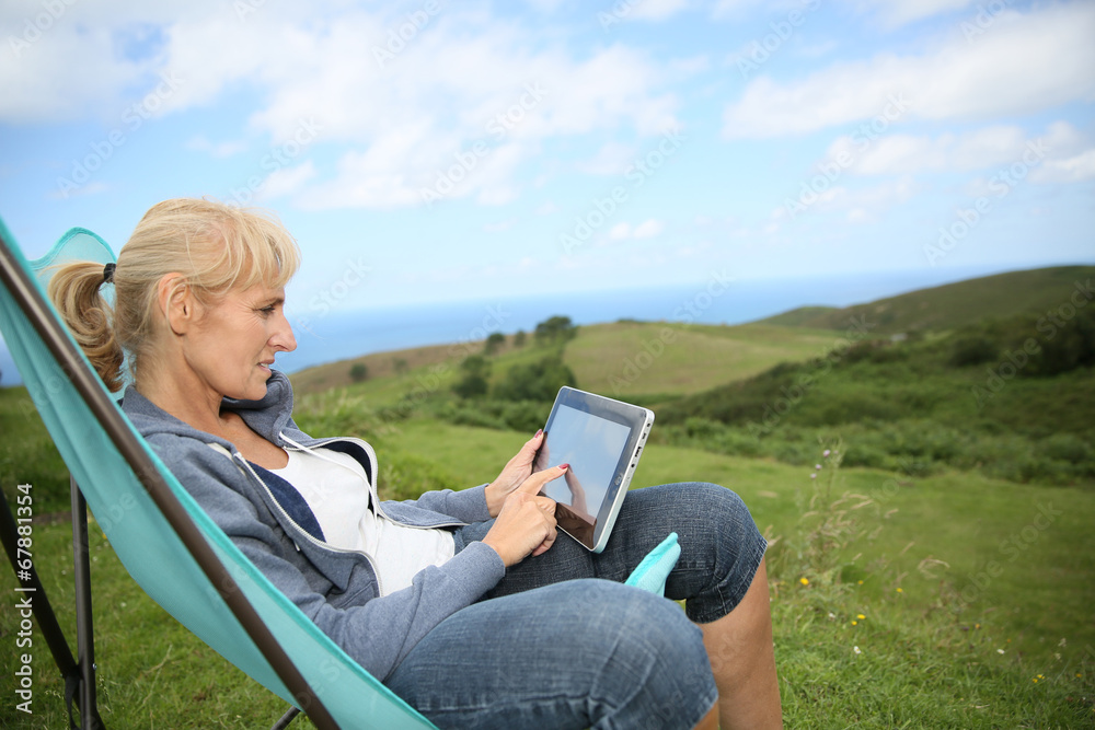 Senior woman weburfing on digital tablet, relaxing in chair