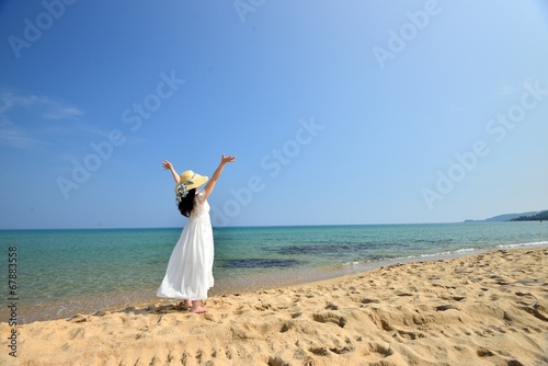 麦わら帽子と白いドレスを着てビーチに立っているアジア人女性の後ろ姿