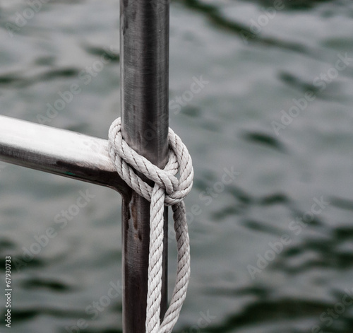 Rope tied to metal railing near water.