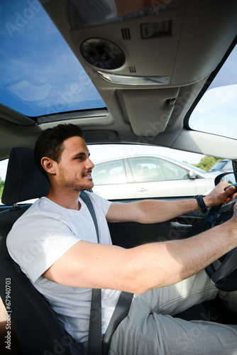 happy handsome young man driving his new car on highway