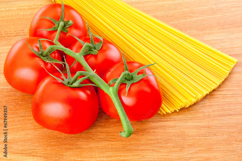 Bunch of spaghetti pasta and ripe tomatoes at branch close-up on