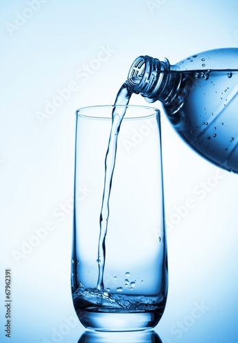 Pouring water into glass from bottle on blue background