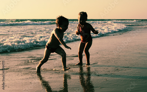 two happy kids playing on the beach at sunset