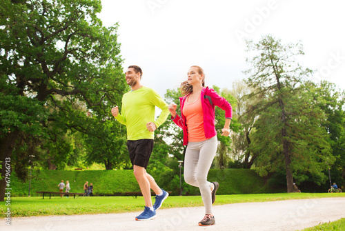smiling couple with earphones running outdoors