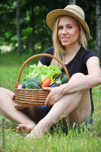 Blond woman sitting holding a basket with vegetables, smiling photo