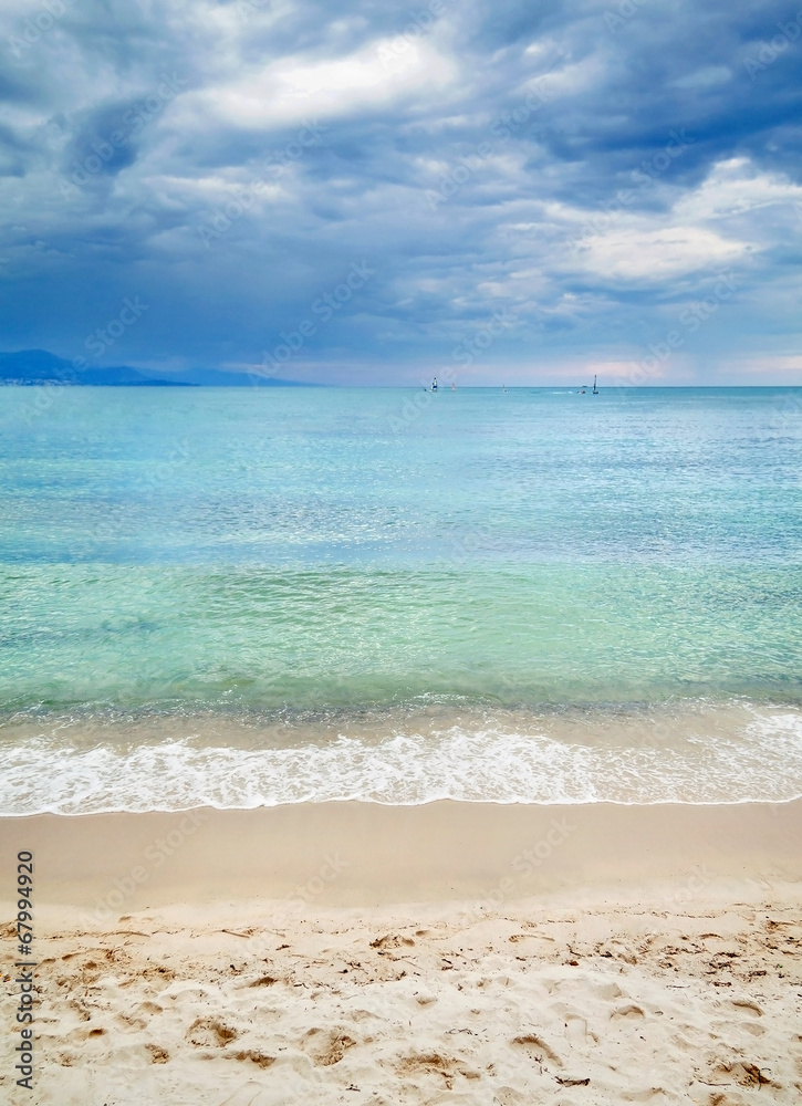 Sandy beach with clean blue waves and cloudy sky.
