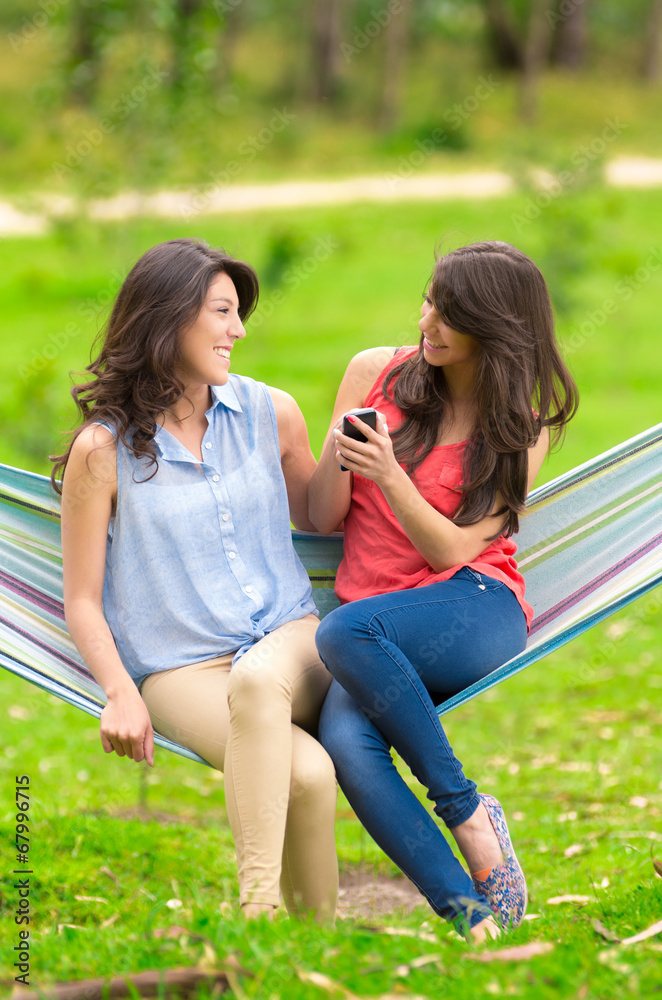 Two young girls resting on a hammock smiling Two young girls resting on a hammock smiling