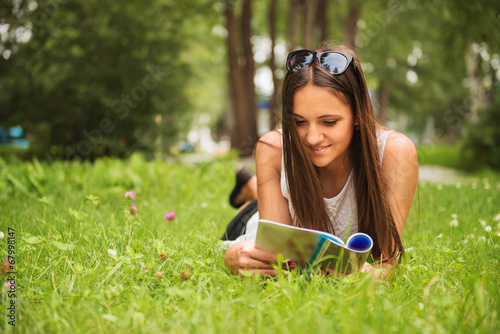 A young brunette woman lying on the grass outdoors with a magazi