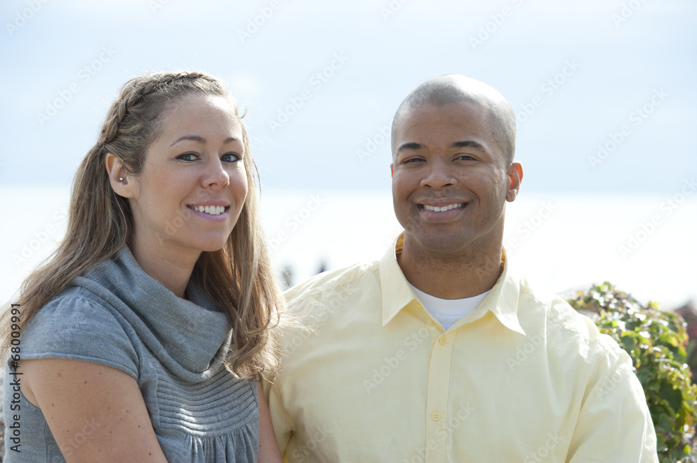 A young and happy interracial couple posing near the beach on a sunny day. A young and happy interracial couple posing near the beach on a sunny day.