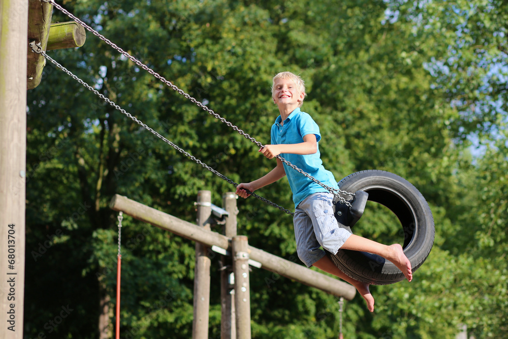 Happy school boy swinging at playground sitting on old tire Happy school boy swinging at playground sitting on old tire