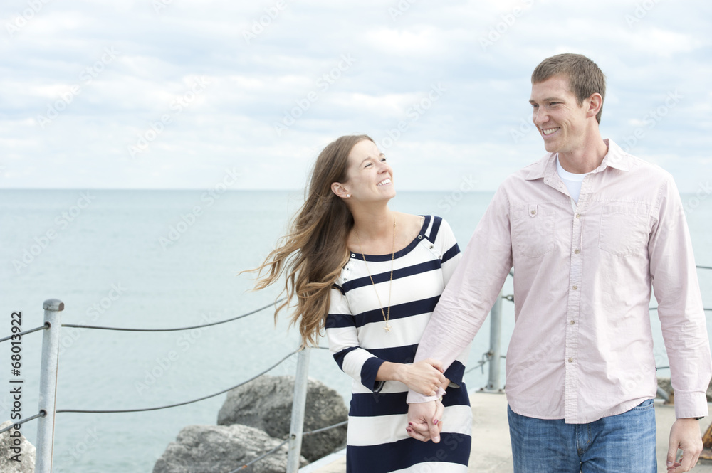 A young happy caucasian couple on a sunny day with the clouds in the background at the pier.