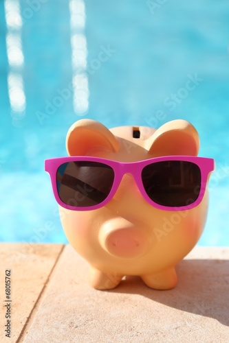 Summer piggy bank with sunglasses in front of a swimming pool © viperagp