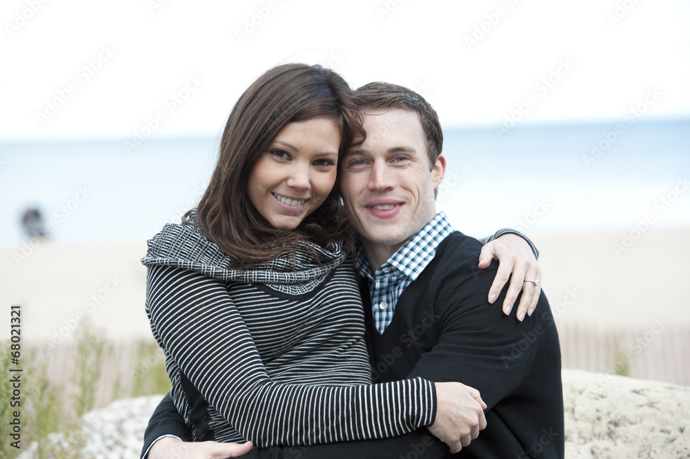 A young and happy couple posing with a beach in the background.