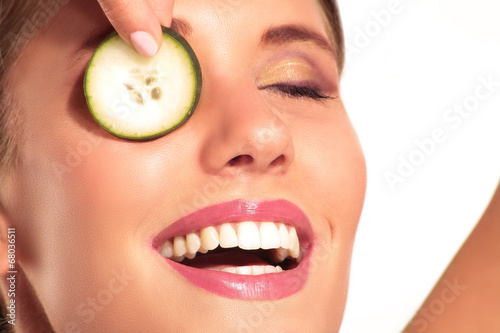 Young beautiflul smiling girl applying a cucumber beauty treatme photo